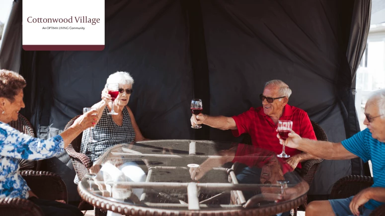 A group of seniors sitting around a patio table toasting with glasses of red wine