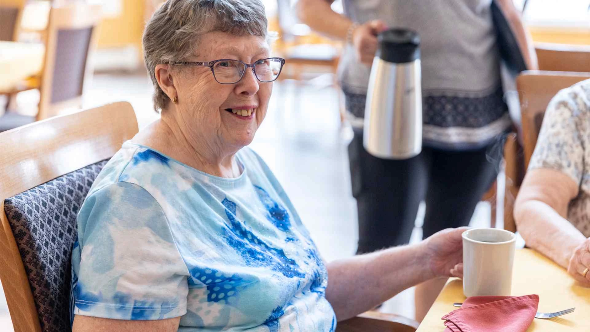 A senior citizen smiling and drinking coffee