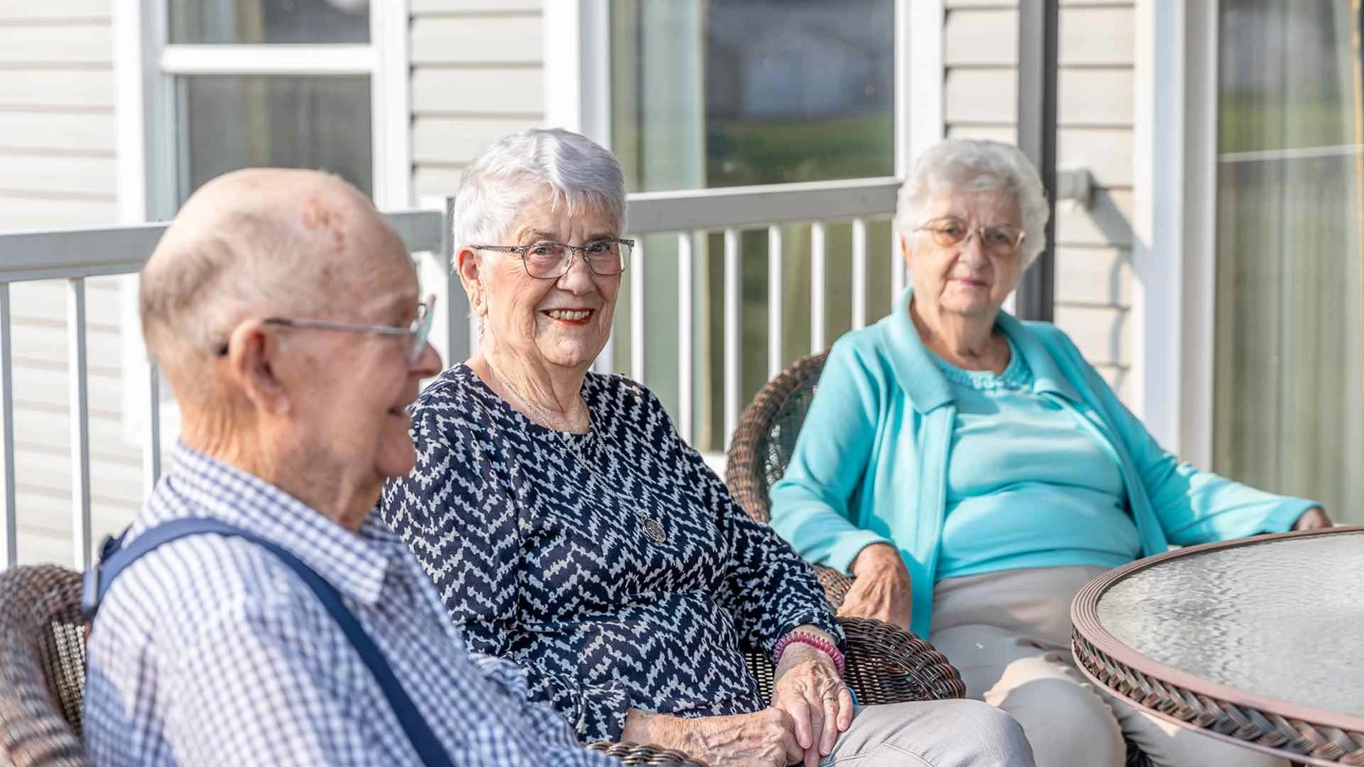 Three elderly people enjoy the sunshine while sitting outside.