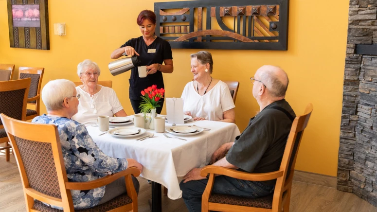 Group of seniors at a table and a worker pouring them coffee